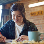 Young Female Carpenter Drawing And Measuring Woodwork Design In Garage Workshop